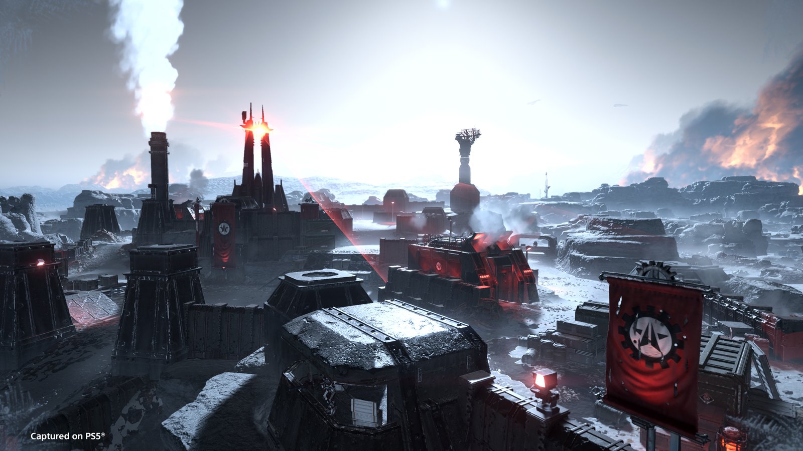 A snowbound Automaton base of dark towers, bunkers and red banners bearing the bot emblem, with smoke and fire on the horizon
