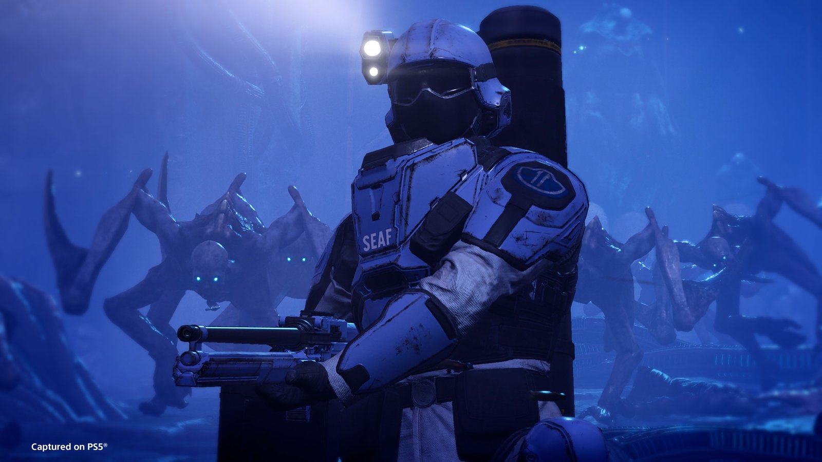 A SEAF trooper with a headlamp and rifle stands in blue light while hunched Wretches with blade arms close in behind