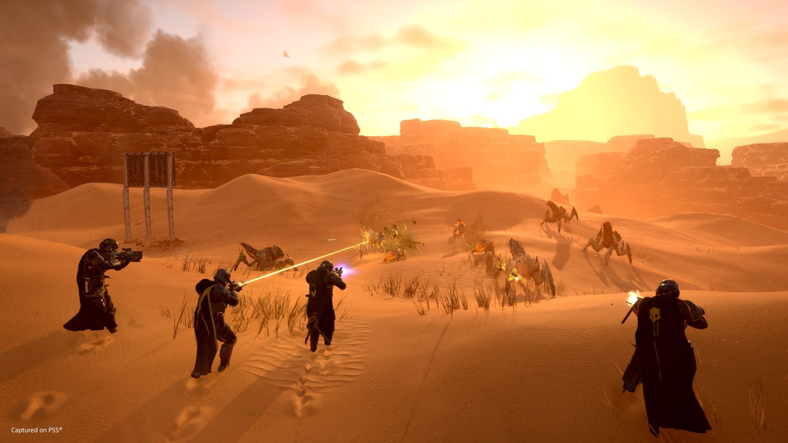Four Helldivers holding a line against Terminids in the desert