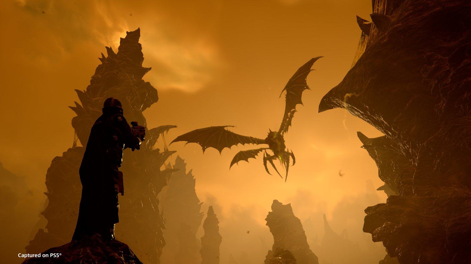 A Dragonroach flies between rock spires under an orange sky as a Helldiver on a ledge aims at it