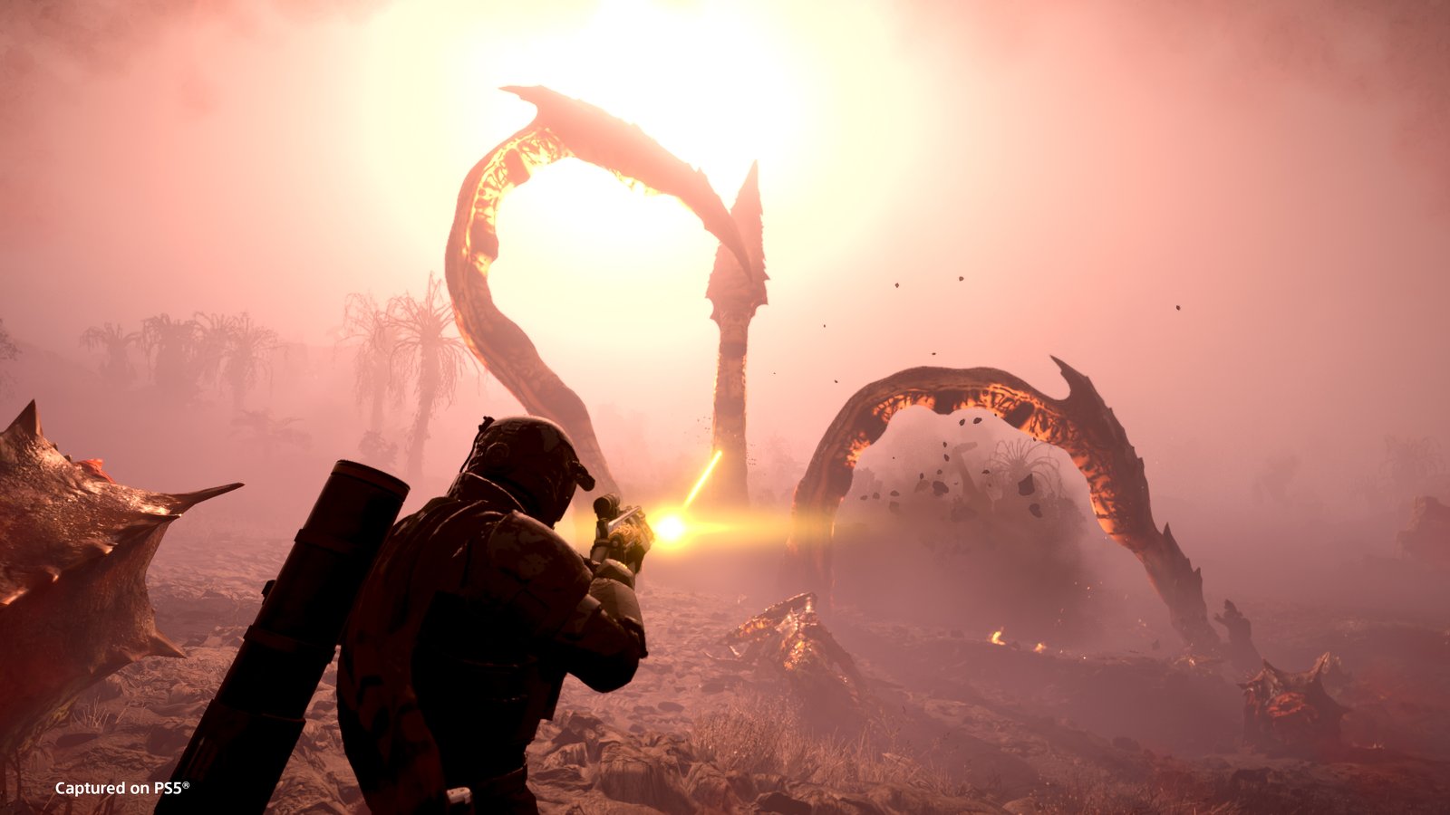 Two of an Impaler's tentacles arch out of the ground in a pink haze as a Helldiver carrying a backpack fires at them