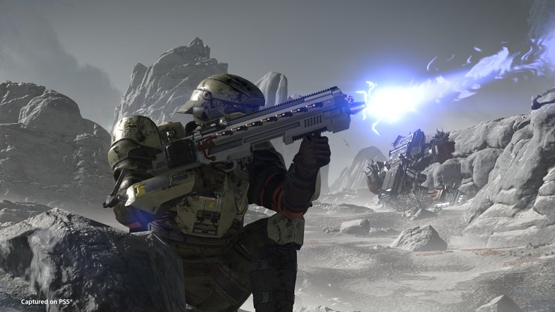 A Helldiver in olive armor fires a blue energy rifle across a gray, rocky world