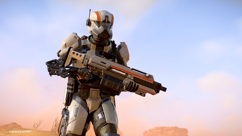 A Helldiver in white-and-orange armor holds the JAR-5 Dominator against a desert sky